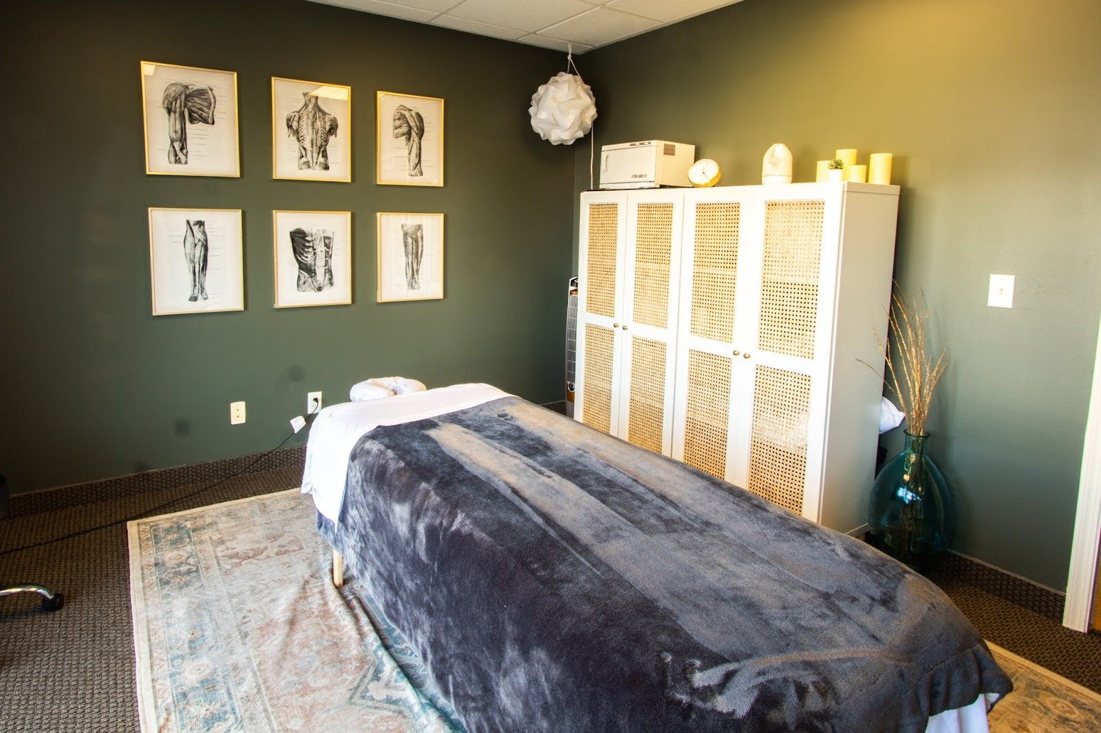 Treatment room with massage table, sage green walls, and framed anatomy prints